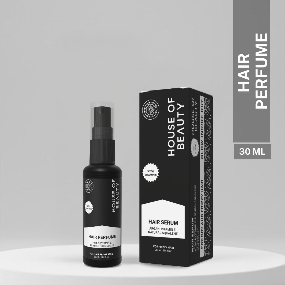 A sleek black bottle of House of Beauty Hair Perfume with packaging, featuring Amla, Vitamin E, and Arabian Rose Oud Oil. The bottle and box are displayed side by side on a minimalist, neutral background.