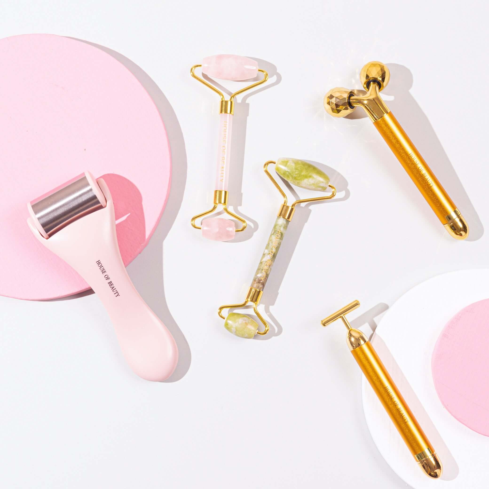 Five beauty products from House of Beauty lying flat featuring a pink ice roller, a rose quartz jade roller , a 3d face massager and a 24 k face massager for fine lines, wrinkes and puffiness.