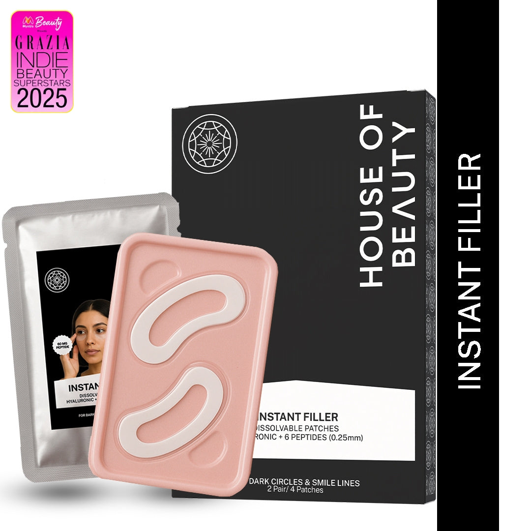 A product shot featuring the House of Beauty Instant Filler Dissolvable Patches. The image shows the black and white outer packaging box, a silver foil patch packet, and the pink case holding the two white, curved patches for under-eyes. Text on the packaging indicates the patches contain dissolvable hyaluronic acid and 6 peptides.