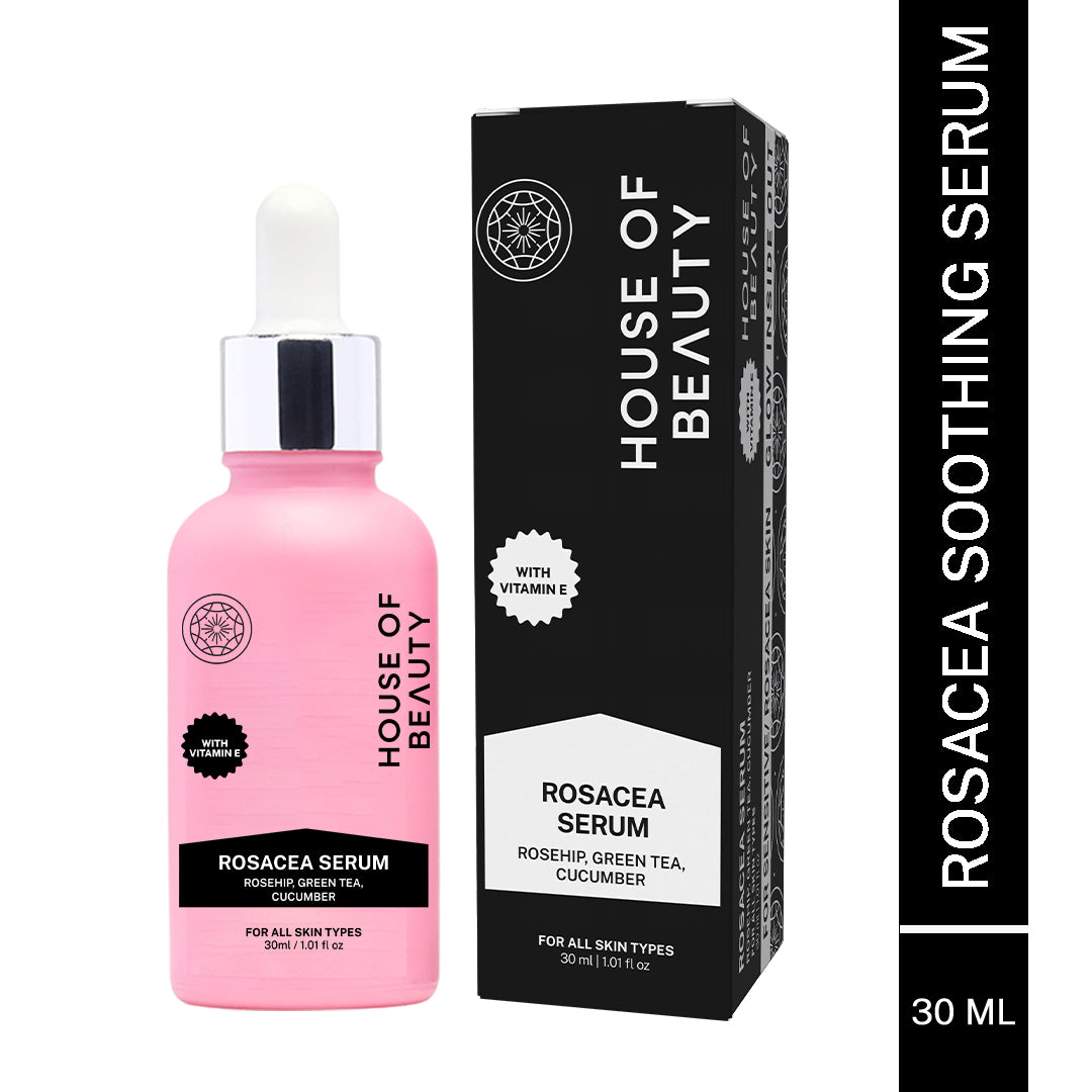 A close-up, high-angle shot of the pink Rosacea Serum bottle lying horizontally on a white surface. Three large, clear droplets of the liquid serum are visible next to the bottle, demonstrating its lightweight, transparent consistency.